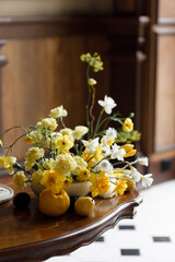 A delicate composition with yellow flowers and fruits, with wedding invitations. Wedding decor in trendy shades, composition on the table with printing.