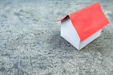 Small toy house with red roof standing gray concrete background.