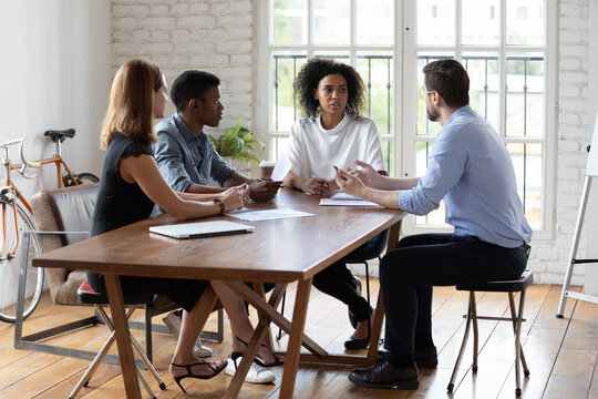 Full Length Motivated Young Mixed Race Business People Sitting At Table, Creating Project Ideas, Discussing Problem Solution, Negotiating Working Issues Or Brainstorming At Group Office Meeting.