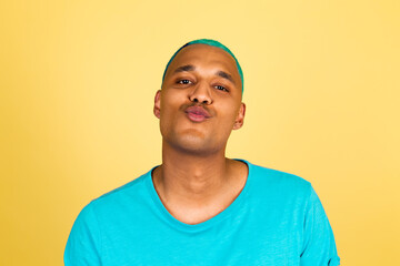 Black african man in casual on yellow background positive look to camera send air kiss