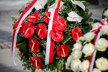 A wreath of red anthurium flowers against the background of the white and red Polish flag during...