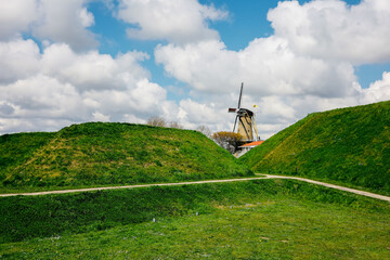 Dutch windmill on top of a lush green field in the Netherlands, cloudy sky background 