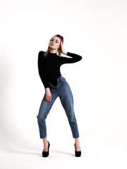 The brunette stands on a white background in a black bodysuit, jeans and high heels