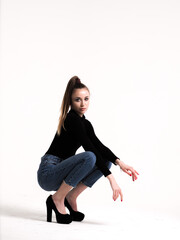 The brunette on a white background in a bodysuit and jeans with heels and a ponytail