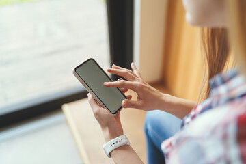 Closeup view of young girl holding a black smartphone while standing near the window