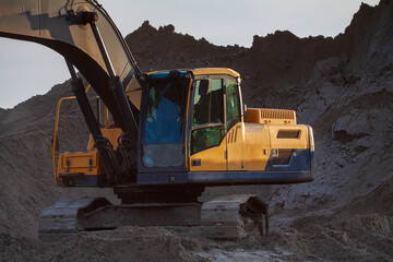 Obraz premium Large construction excavator yellow on a construction site in a quarry for quarrying. Yellow excavator on a construction site against blue sky.