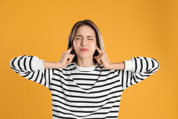 Emotional young woman covering her ears with fingers on yellow background