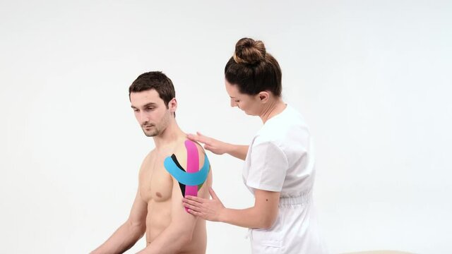 Shoulder treatment with kinesio tape. Physiotherapist applying elastic therapeutic tape to patient shoulder injury