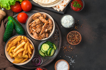 French fries, fried meat, cucumbers, tomatoes and lettuce on a brown background with space to copy. Lunch, or ingredients for shawarma, burritos, gyros.