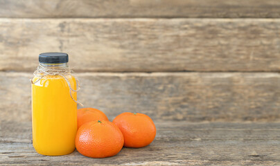 A bottle of tangerine juice and whole tangerines on wooden background