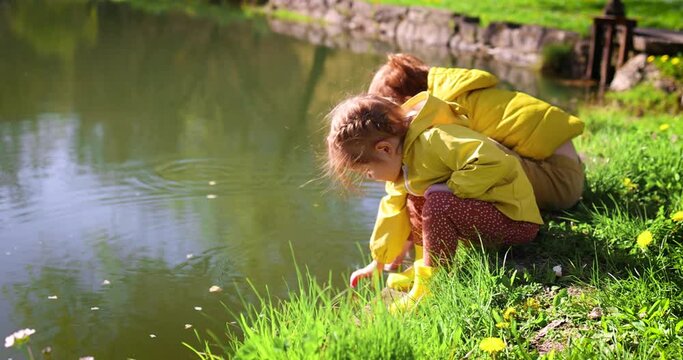 cheerful siblings, kids are sitting by the pond, feeding fish and playing with water on sunny day