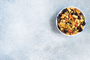 A mixture of nuts and dried fruits in a ceramic plate on a gray concrete background. Concept of healthy food. Copy space