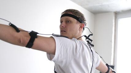 athletic man with beard wears motion capture suit with sensors headset moving in virtual reality taking something and looking at his hands excited experience cyber space online