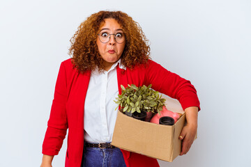 Young curvy woman moving to a new home isolated on white background shrugs shoulders and open eyes...