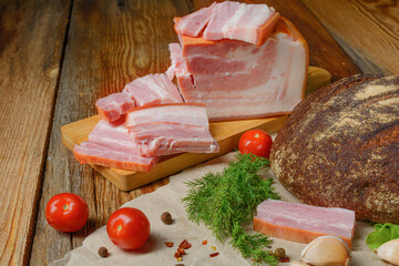 Smoked sliced pork belly, bacon, ham with herbs, tomatoes and black pepper on food paper. Wooden rustic background.Selective focus.