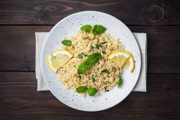 Boiled bulgur with fresh lemon and mint on a plate. A traditional oriental dish called Tabouleh. dark wooden background. top view, copy space