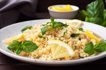 Boiled bulgur with fresh lemon and mint on a plate. A traditional oriental dish called Tabouleh. dark wooden background.
