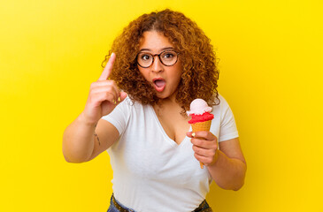 Young latin woman holding an ice cream isolated on yellow background having an idea, inspiration concept.