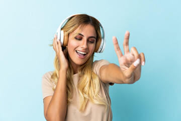 Fototapeta premium Young blonde Uruguayan isolated on blue background listening music and singing