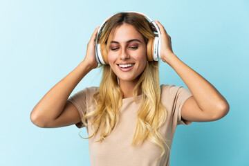 Naklejka premium Young blonde Uruguayan isolated on blue background listening music