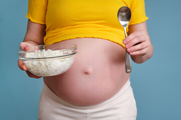 A plate with cottage cheese in the hands of a pregnant woman on a blue background