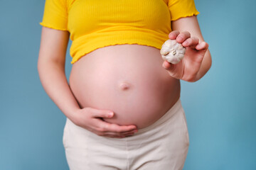 A garlic bulb in the hands of a pregnant woman on a blue background