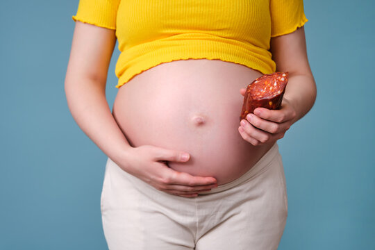 Meat sausage in the hands of a pregnant woman on a blue background