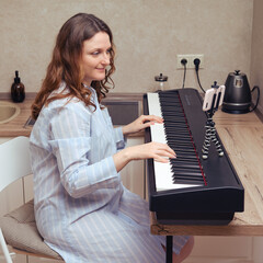 A pregnant woman in a blue nightie plays the piano. Music lessons in home kitchen close up