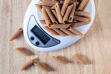A portion 50 gm of pasta  Penne on a kitchen scales, flat lay