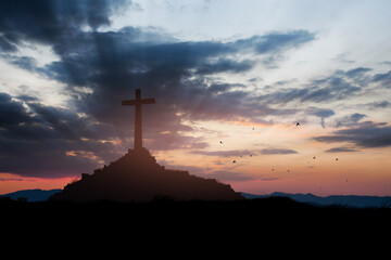 Concept conceptual black cross religion symbol silhouette in grass over sunset or sunrise sky.