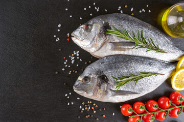 Fototapeta na wymiar Fresh fish dorado on black slate background with ingredients for cooking