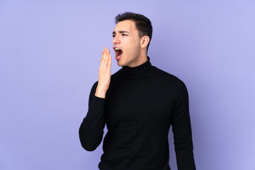 Young caucasian handsome man with turtleneck sweater isolated on purple background yawning and covering wide open mouth with hand