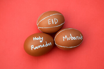 Fototapeta na wymiar Holy Ramadan and Eid Mubarak hand typography on the egg. Red isolated background.