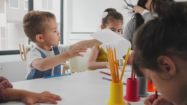 Boy handing over a paper to the teacher in the kindergarden.