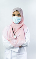 Muslim female doctor wearing headscarf, gown uniform and face mask to protect virus with stethoscope, crossing arms with confidence on isolated white background. New Normal, Medical Treatment Concept.