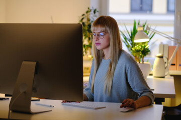 Cosy office room and beautiful woman using a computer in evening