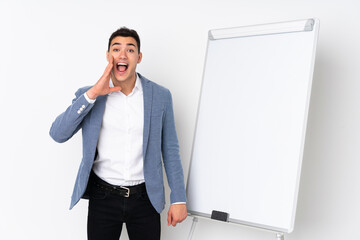 Young caucasian handsome man isolated on purple background giving a presentation on white board and shouting with mouth wide open