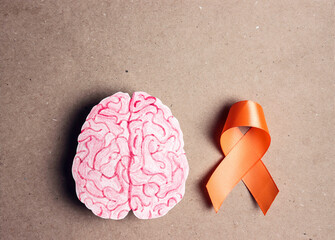 Orange awareness ribbon and brain symbol on a brown background.