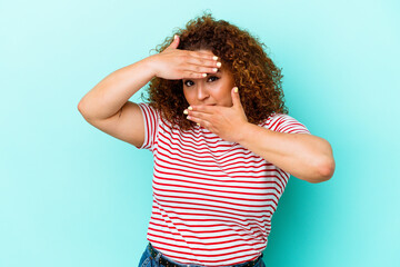 Young latin curvy woman isolated on blue background blink at the camera through fingers, embarrassed covering face.