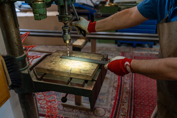 metal worker drilling holes in metal with a bench drill