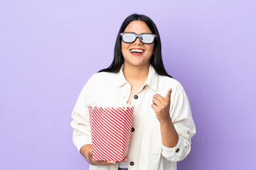 Young latin woman woman isolated on white background with 3d glasses and holding a big bucket of popcorns while pointing front