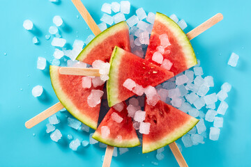 Watermelon slices popsicles and ice on blue background