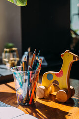 Wooden toy giraffe, colored pencils and a coloring book on a wooden table.