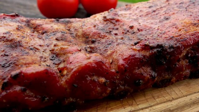 Super close-up panorama of the juicy grilled ribs on the skewers laying on the wooden board on the background of the tomatoes