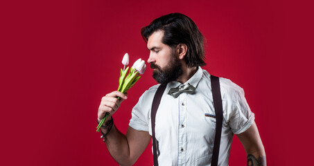 handsome hipster hold tulip bouquet. fathers day. mature retro man. bearded man in suspenders smell flowers. brutal guy ready for romantic date. elegant male with floral present