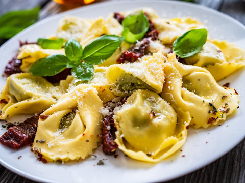 Tortelloni stuffed with ricotta cheese, basil pesto and vegetables on wooden table
