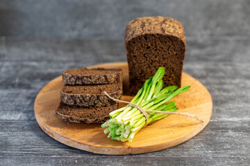 Bouquet of freshly picked green leaves of wild garlic on a gray background with bread and salt. Healthy green leeks or wild garlic leaves