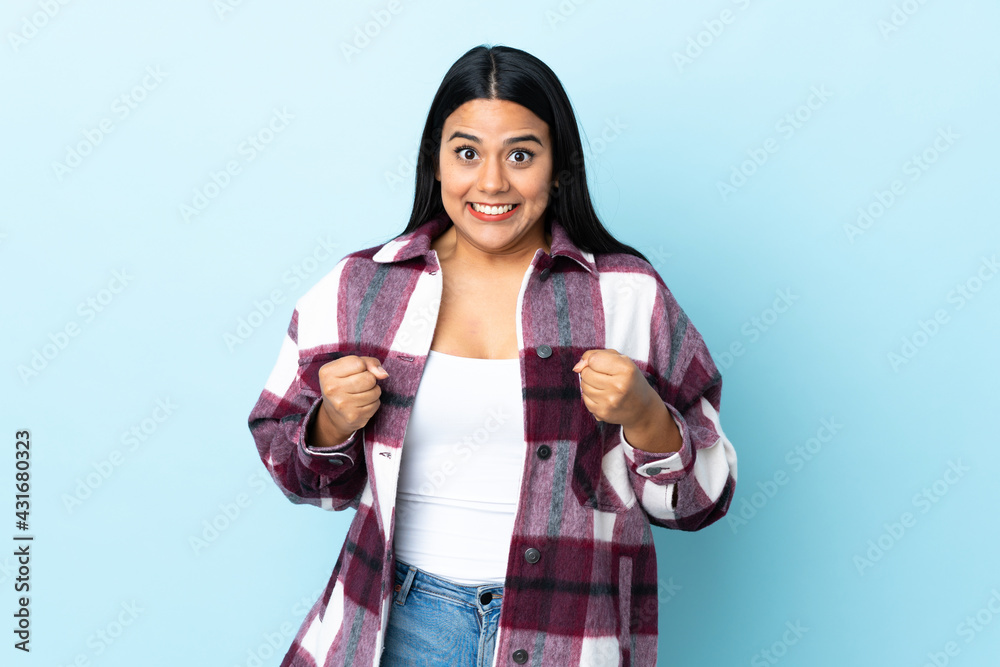 Wall mural Young latin woman woman isolated on blue background celebrating a victory in winner position