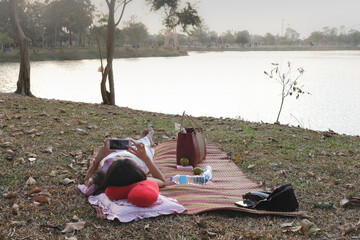 Woman relax on mat and take photo at the park near the pond
