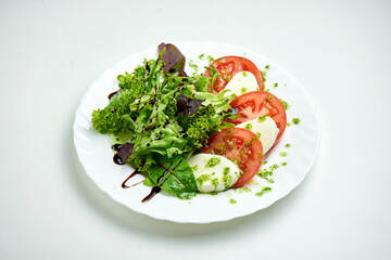 Classic Italian caprese salad with tomatoes, mozzarella, mix salad and pesto sauce in a white plate on a white plate